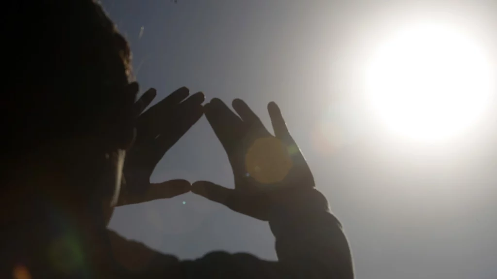 Una persona levanta las manos hacia el sol.